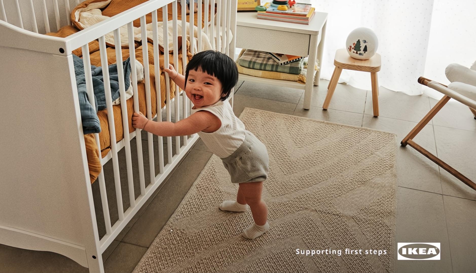 Un bebé asiático apoyándose en una cuna mientras aprende a andar