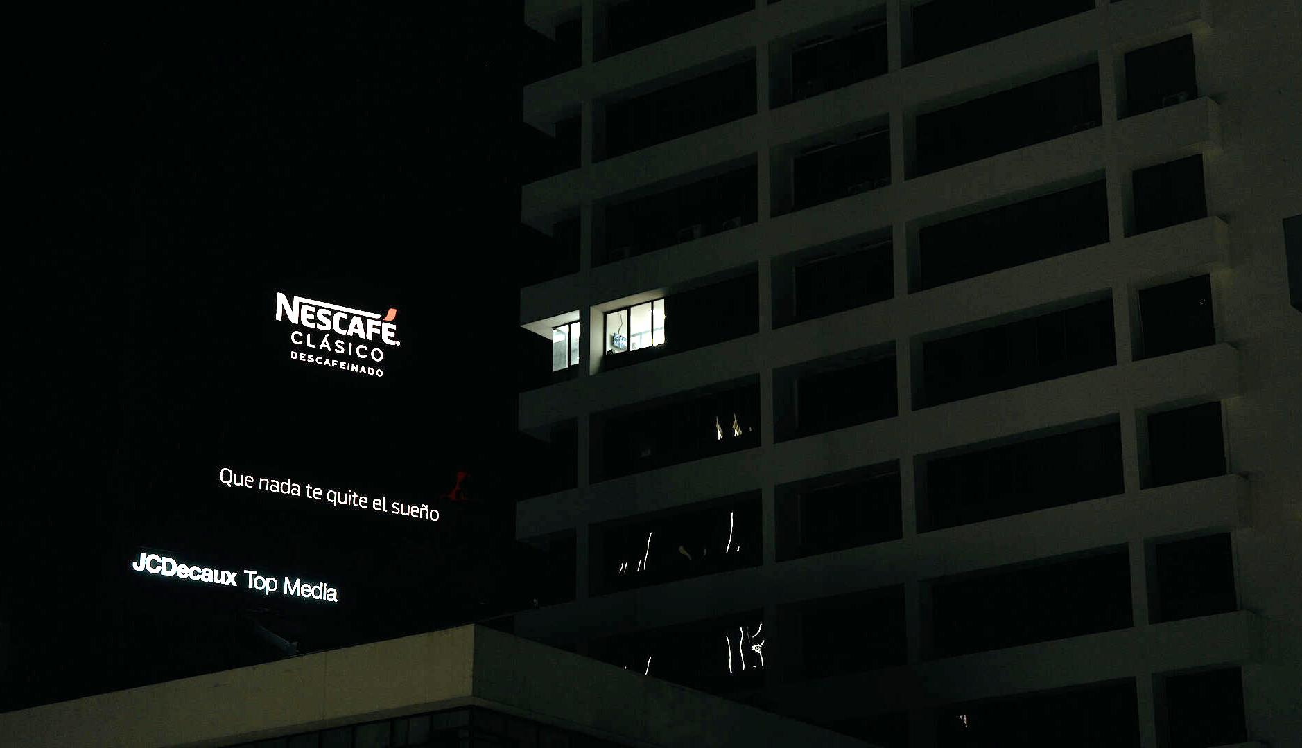 Valla publicitaria de Nescafé por la noche frente a un edificio de viviendas