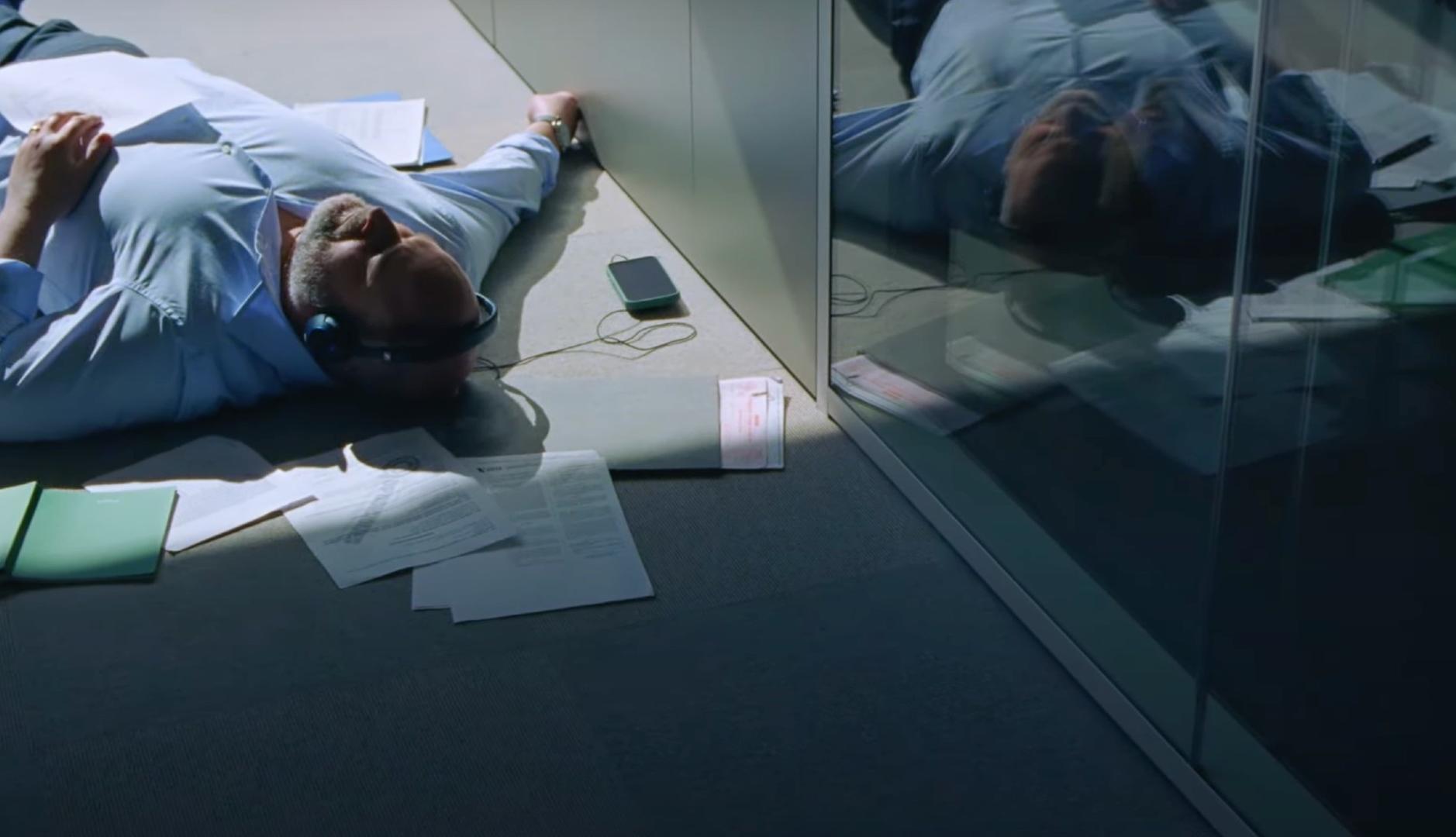 Directivo tumbado en el suelo de su oficina escuchando musica