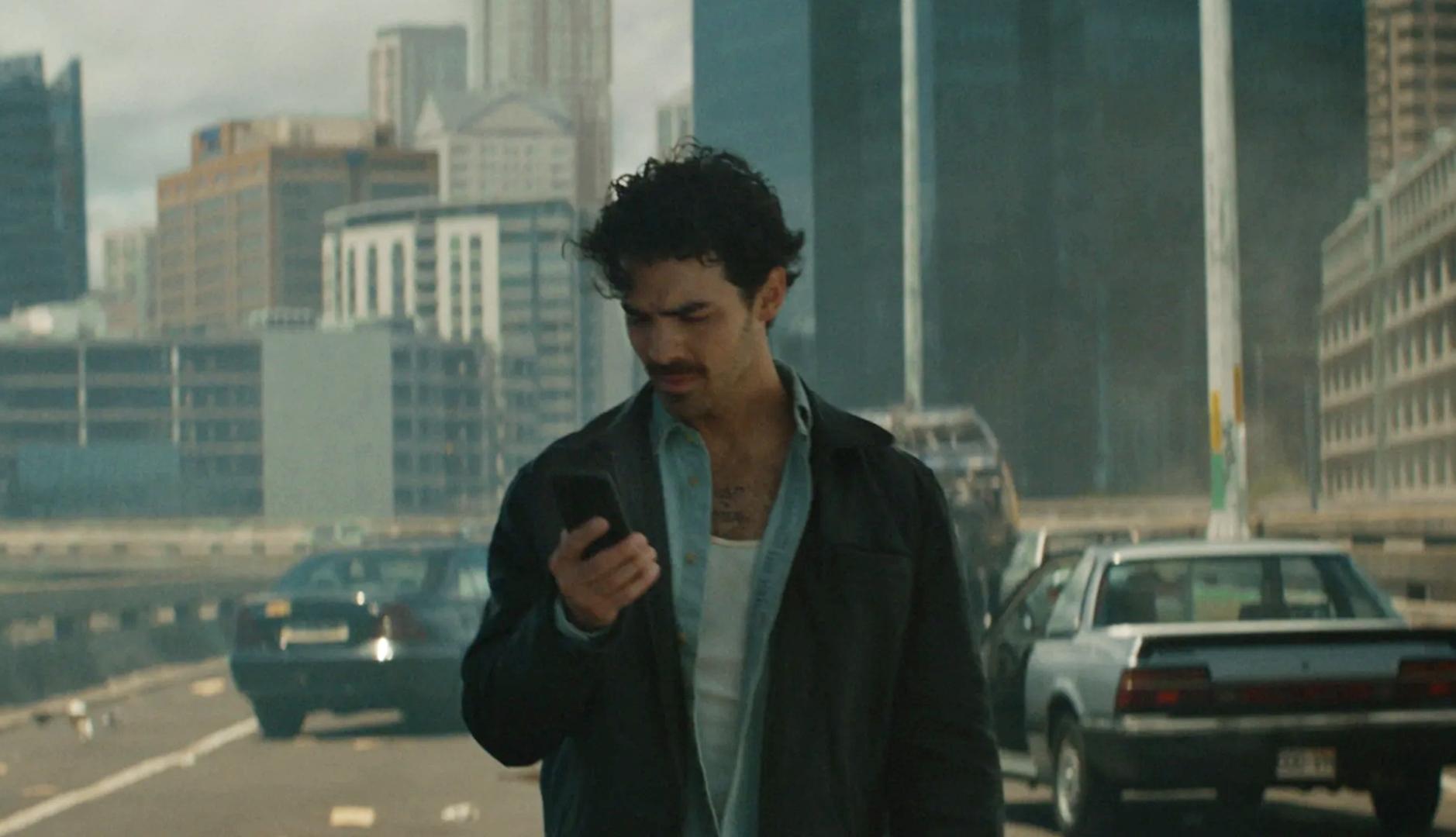 Joe Jonas mirando un teléfono móvil en una ciudad arrasada y sin habitantes
