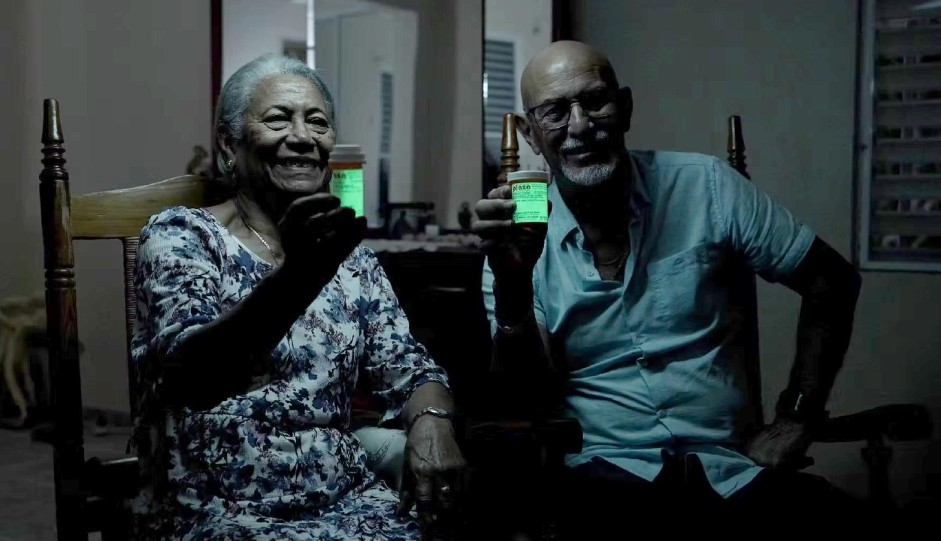 una pareja de personas mayores mostrando el bote de medicamentos con la etiqueta que brilla en la oscuridad