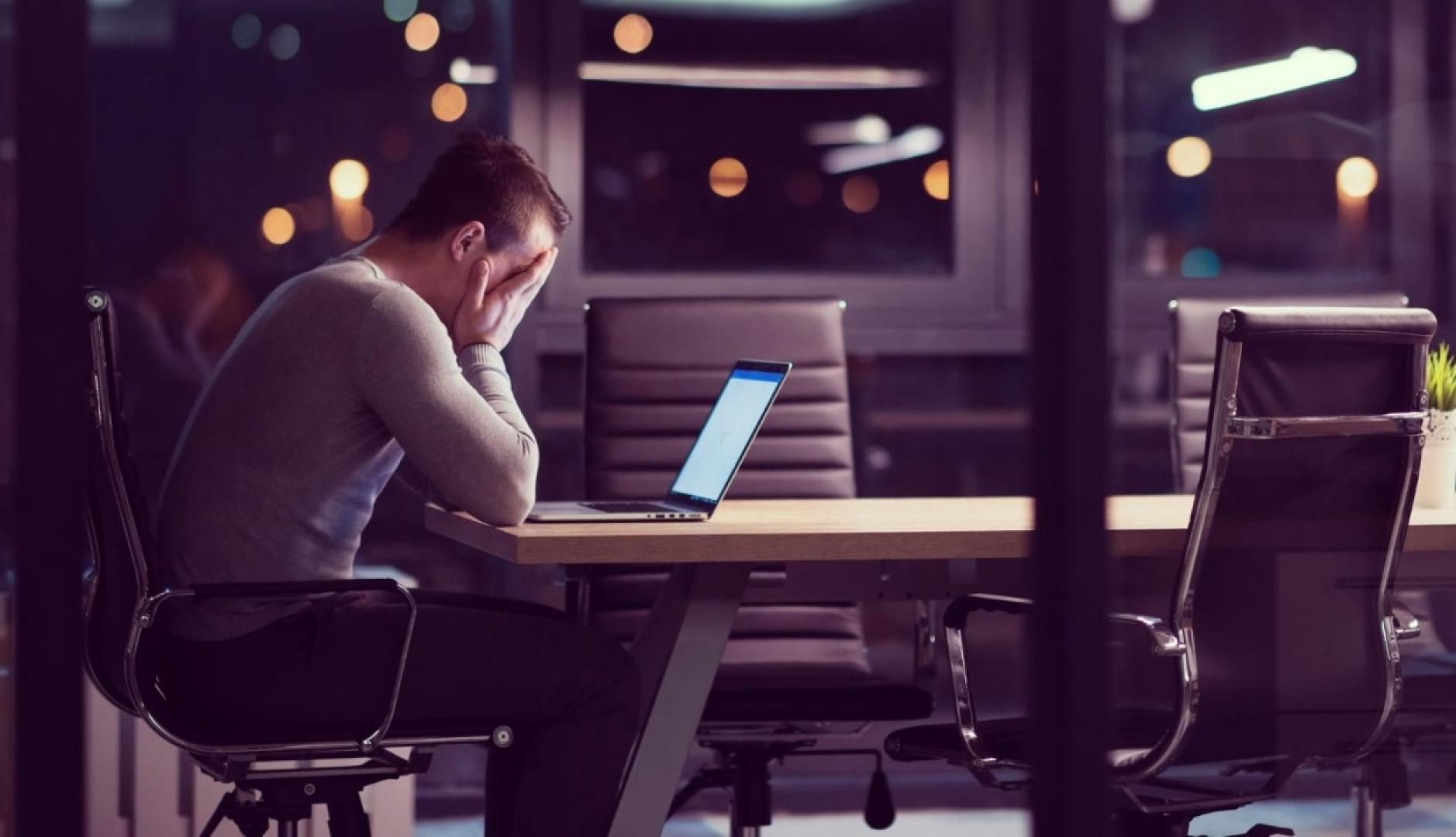un hombre de noche en una sala de reuniones, él solo se echa las manos a la cara en un gesto de desesperación frente al portátil
