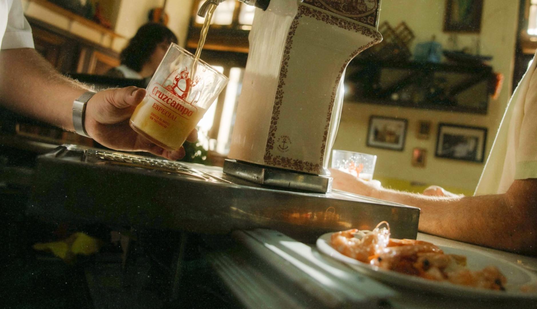 una camarero tirando una cerveza de grifo en un bar junto a un plato de gambas