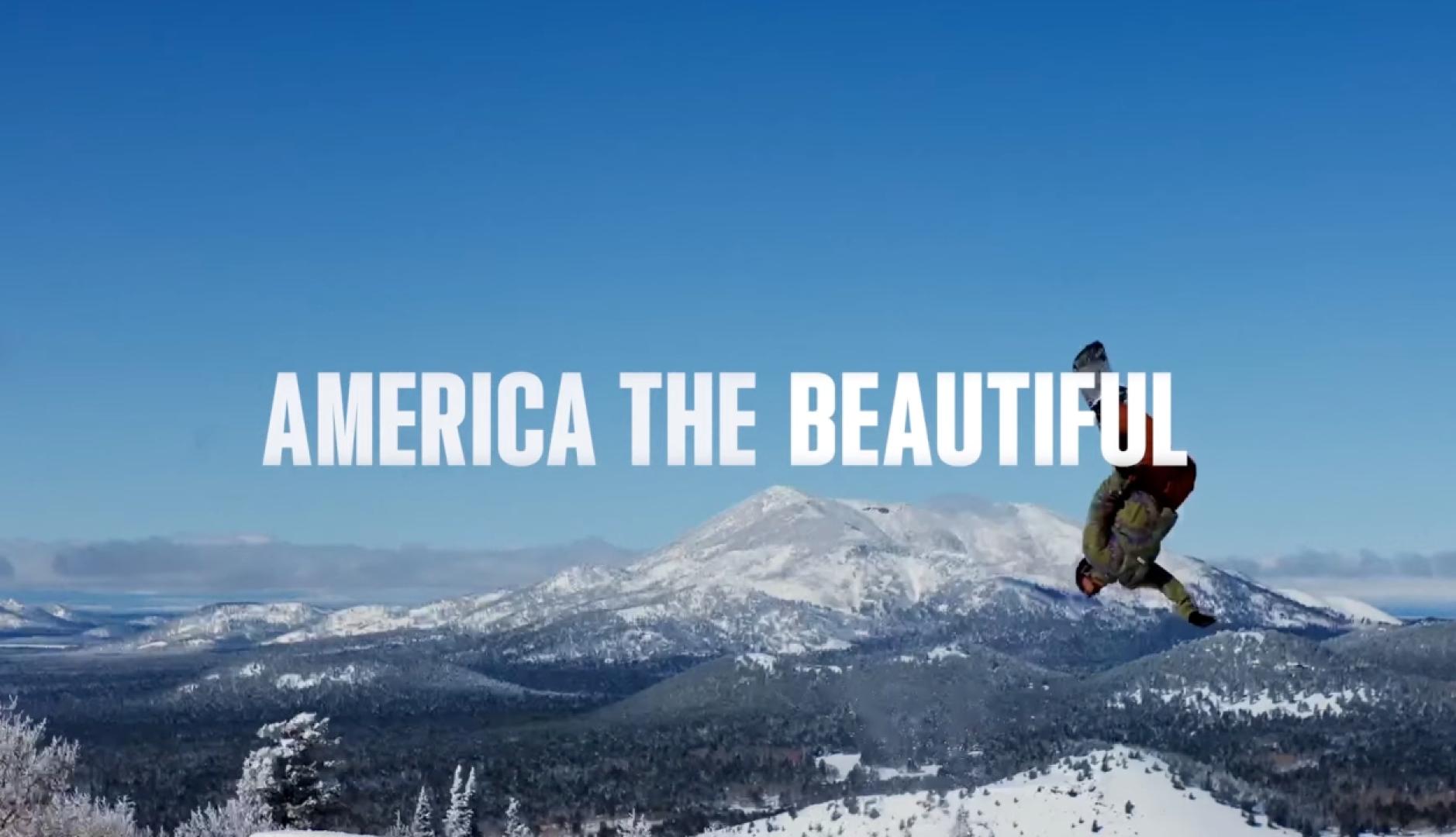 Un hombre haciendo snowboard en la nieve con las letras sobreimpresas de "America the beautiful"