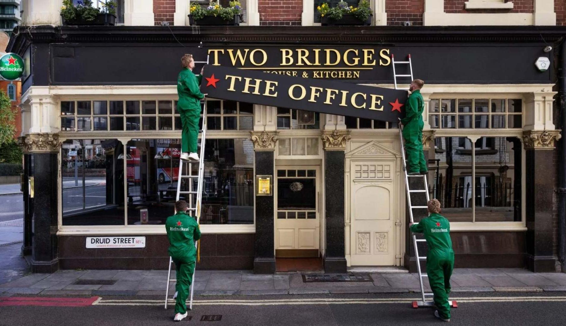 Trabajadores con monos de Heineken colocan un cartel en la fachada de un pub