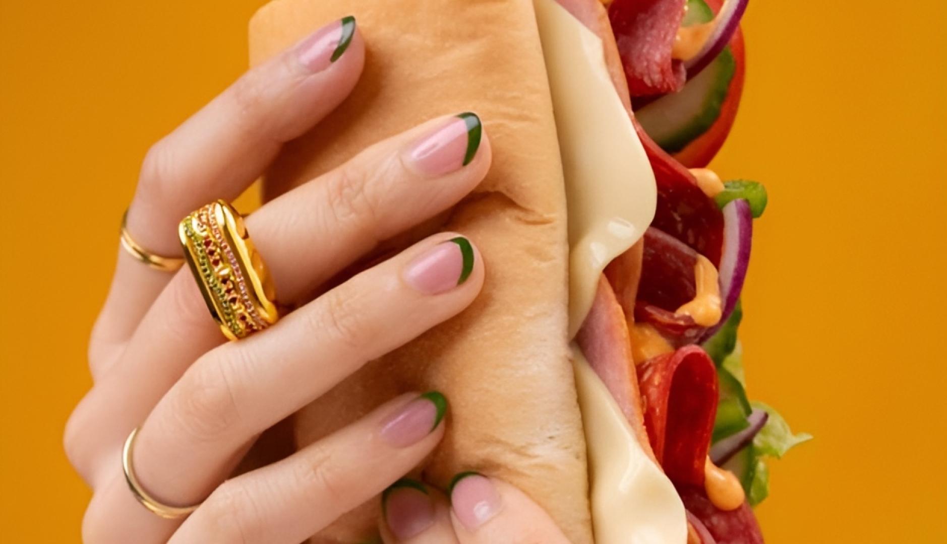 Unas manos sosteniendo el sándwich de Subway y en un dedo puede verse el anillo de oro con forma de baguette