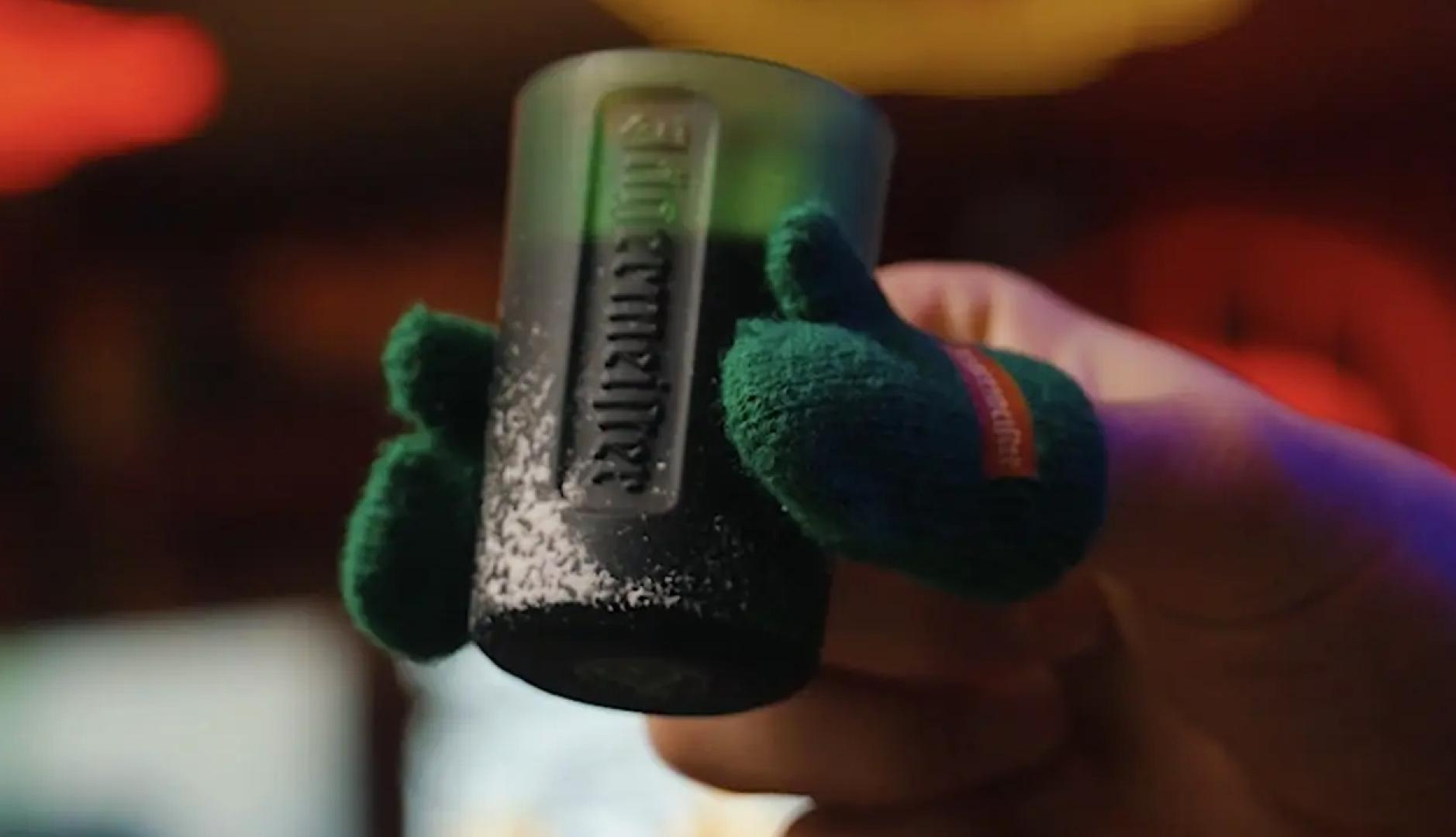 Una mano sosteniendo un chupito con guantes en el dedo pulgar e índice