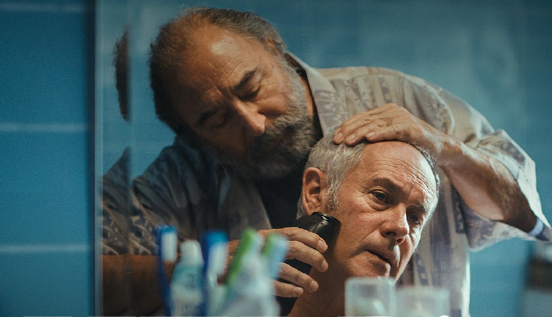 Un hombre pasando la maquinilla de afeitar a otro por la barba