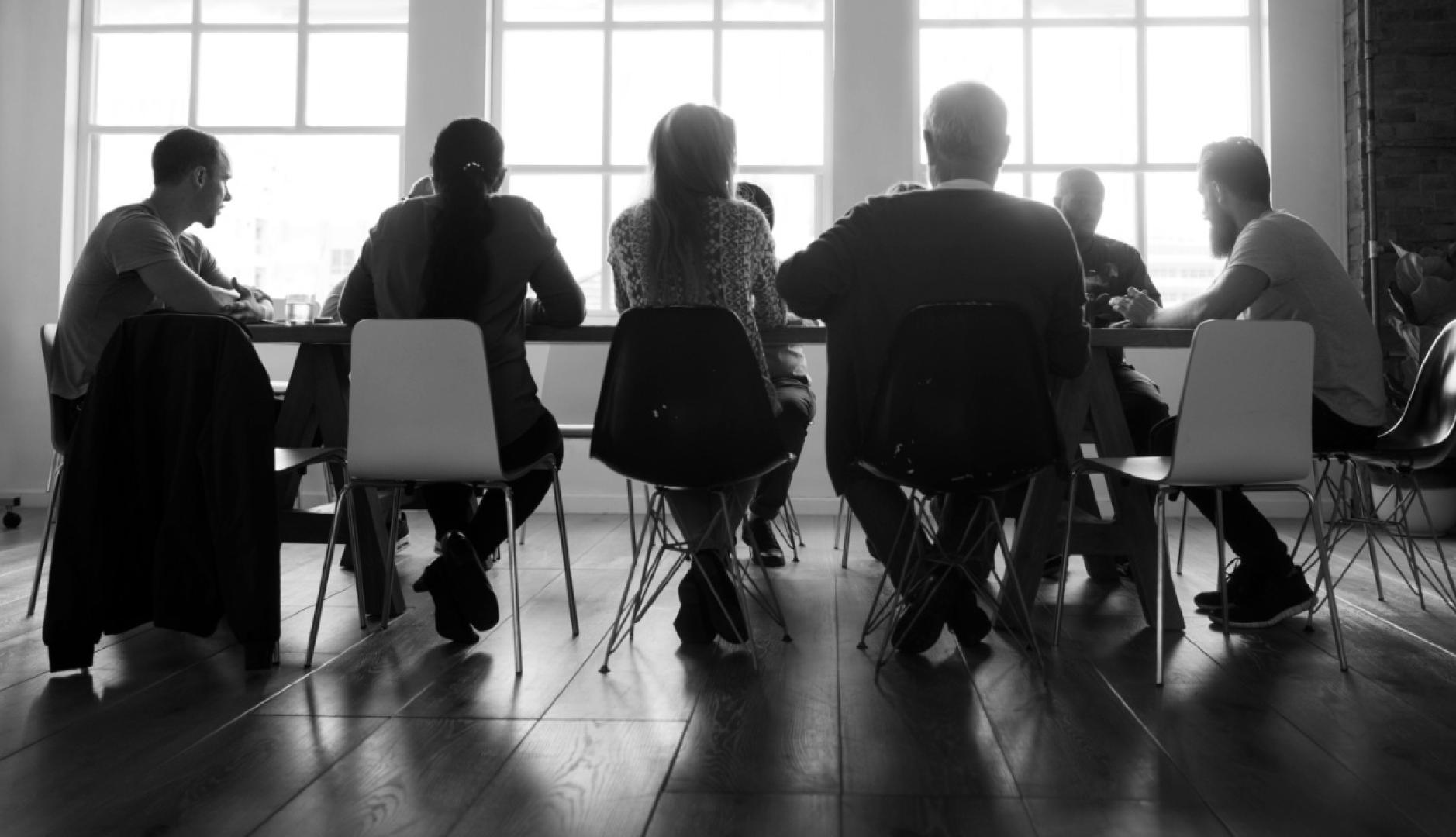 Una imagen en blanco y negro de personas reunidas en una mesa de oficina