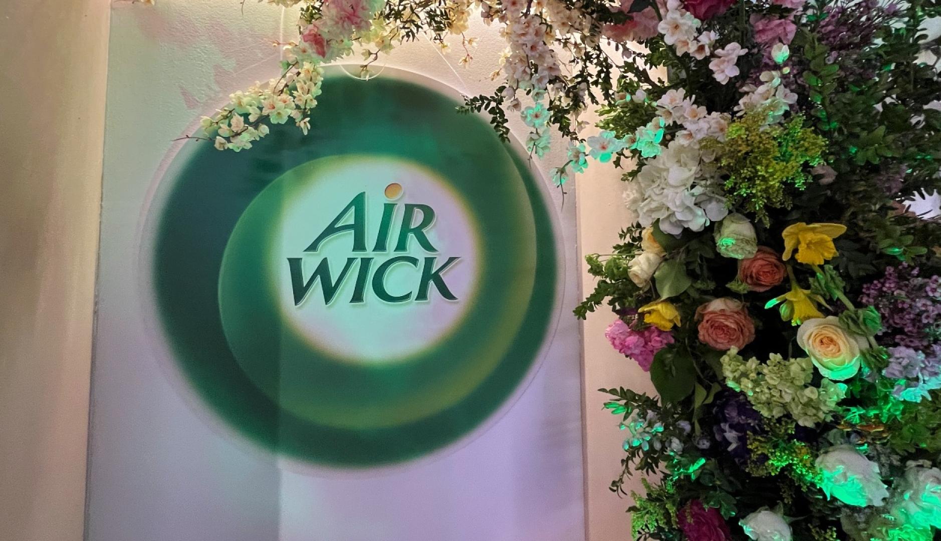 El logotipo de Air Wick junto a una pared de flores de colores