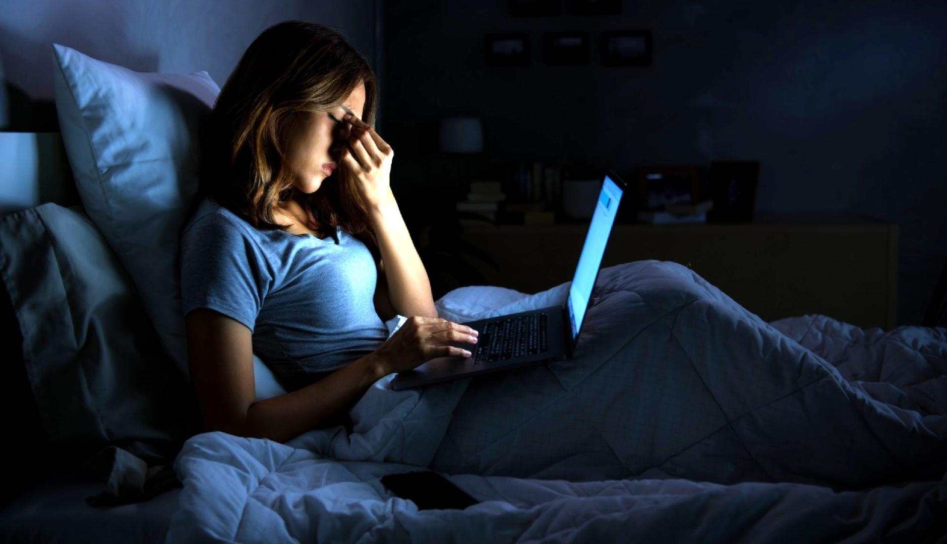 Una mujer en la cama con gesto de preocupación sosteniendo el portátil en las piernas